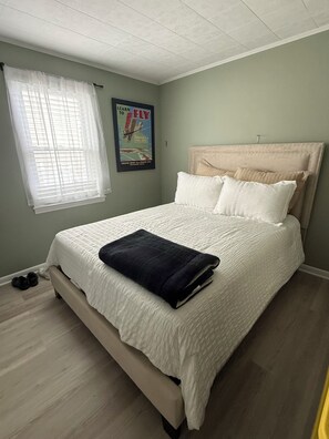 A bedroom with a bed, a window with blinds, a poster on the wall, and a pair of shoes on the floor.