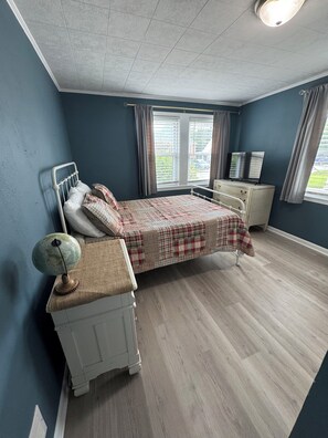 A bedroom with a bed, bedside table, lamp, and curtains.