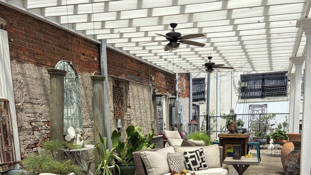 An outdoor patio with wooden furniture, potted plants, and a brick wall.