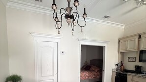 A living room with a chandelier, a sofa, a coffee table, and a kitchen area with cabinets and appliances.