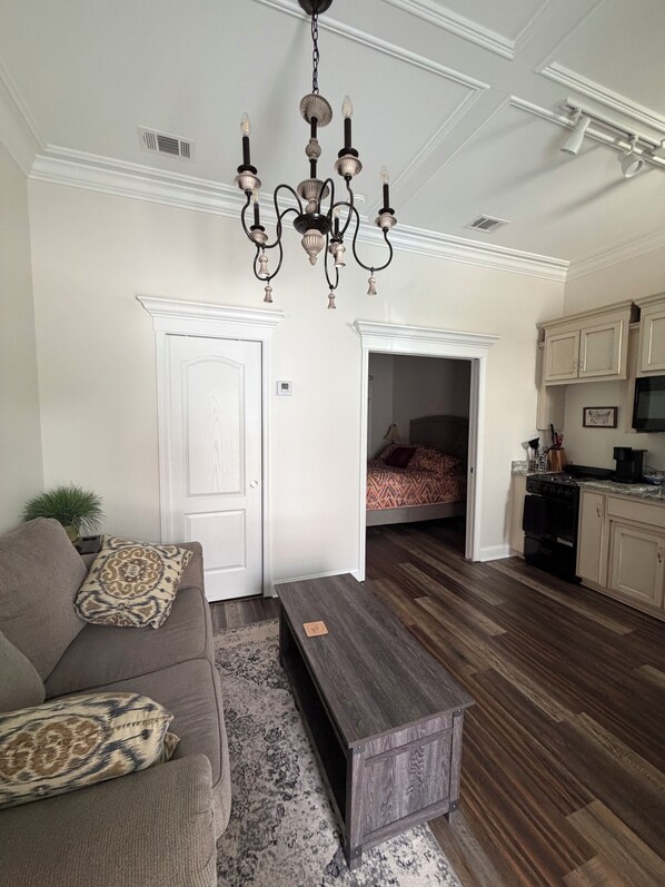 A living room with a chandelier, a sofa, a coffee table, and a kitchen area with cabinets and appliances.