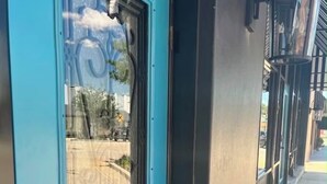 A blue door with a keypad lock and a glass panel reflecting a street view.