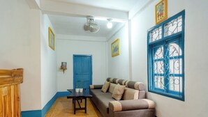 A room with a sofa, a table, a blue door, and a window with decorative bars. - Keokhounmuang Hostel (Luang Prabang)