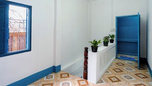 A hallway with a blue door, a white reception desk with potted plants, and patterned floor tiles. - Keokhounmuang Hostel (Luang Prabang)