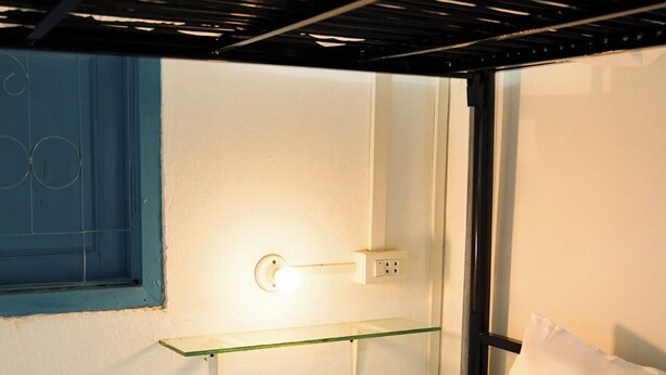 A bunk bed with a shelf above it, a wall socket, and a window with a blue frame. - Keokhounmuang Hostel (Luang Prabang)