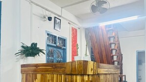 A reception desk with a wooden finish, a potted plant, and a staircase in the background. - Keokhounmuang Hostel (Luang Prabang)