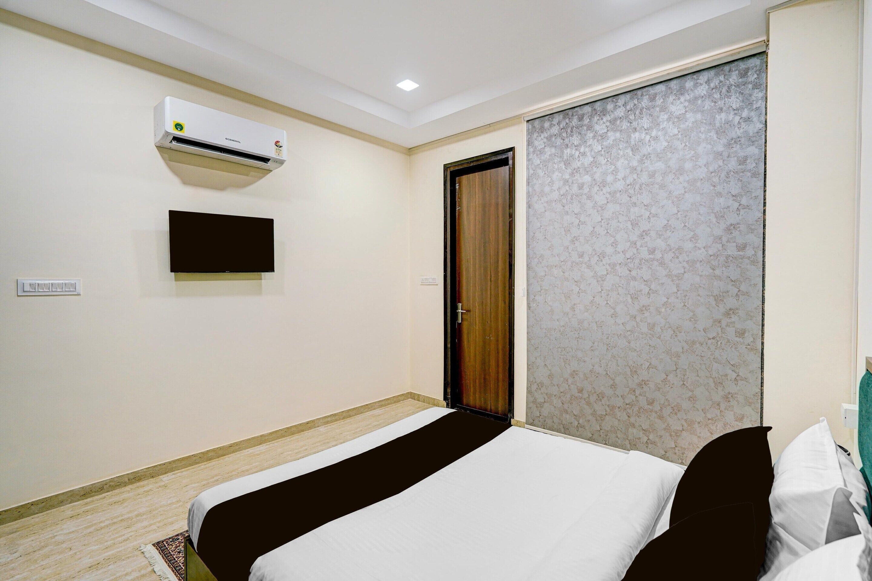 A hotel room with a bed, a wall-mounted air conditioner, a flat-screen TV, and a sliding door.