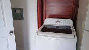 A front-loading Samsung washer in a room with a wooden door and a white wall.