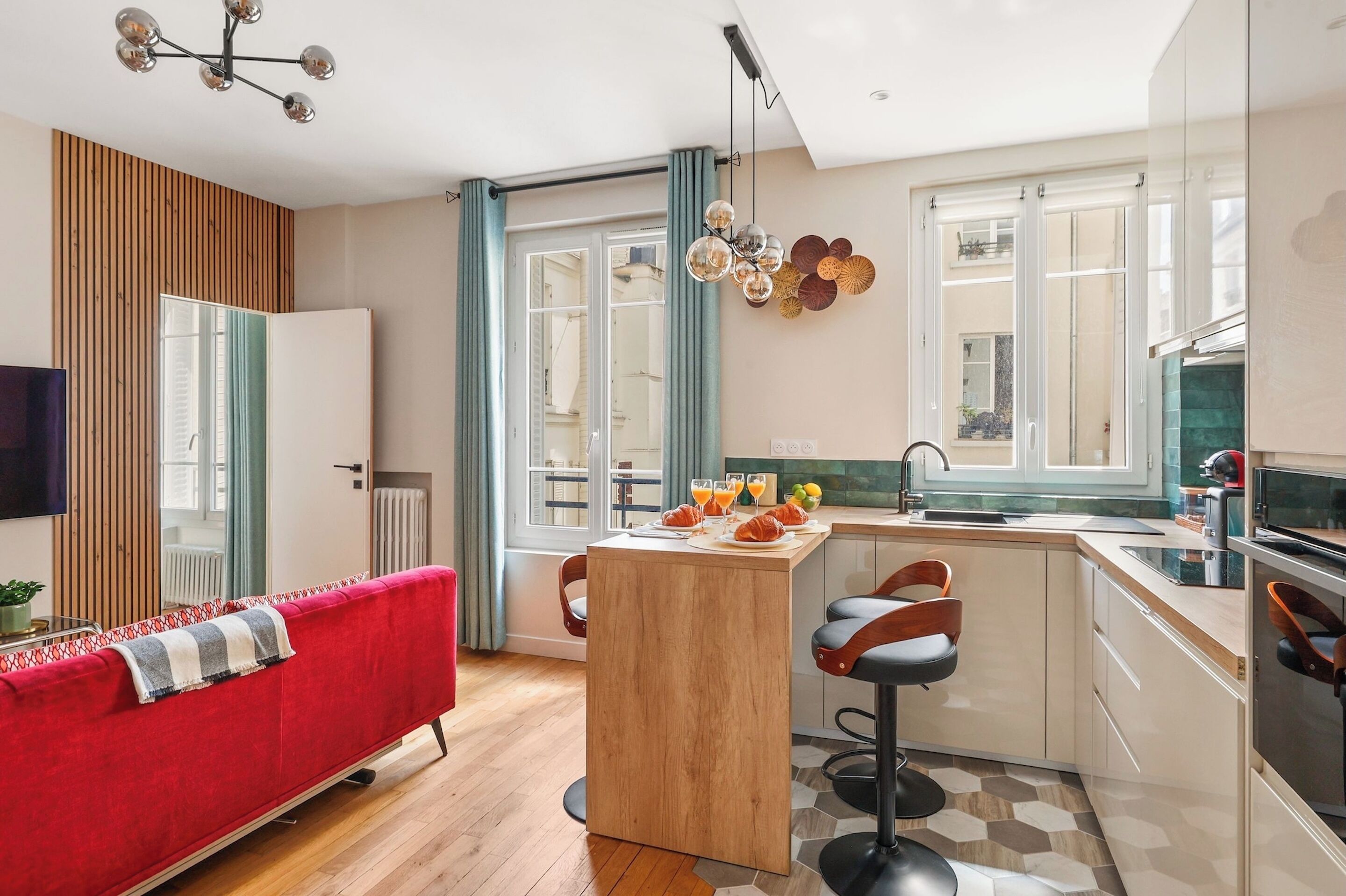 A modern apartment with a red sofa, wooden flooring, a kitchen with a bar area, and a dining table with breakfast items.