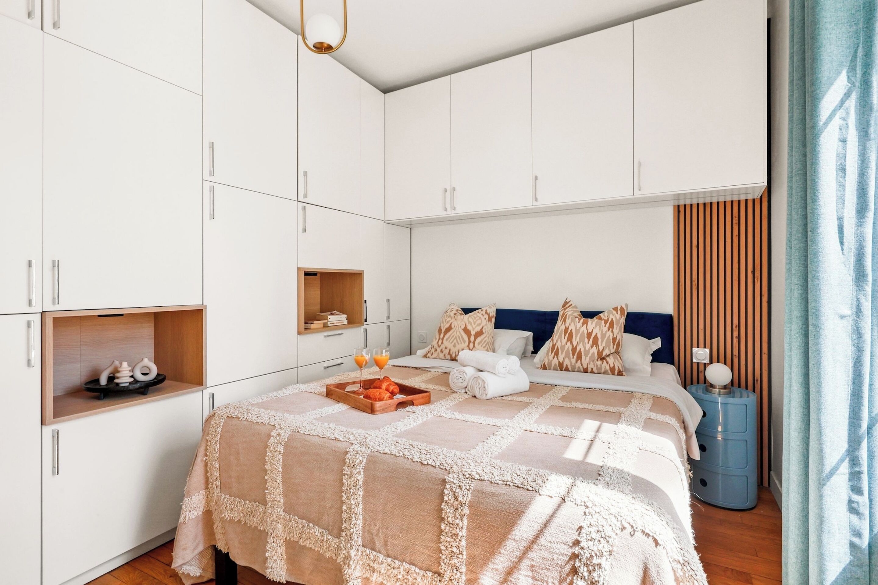 A bedroom with a bed, a bedside table, a wardrobe, and a small shelf.