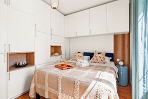 A bedroom with a bed, a bedside table, a wardrobe, and a small shelf. - Chic Flat near Opéra & Marais (Paris)