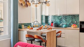 A modern kitchen with a herringbone tile backsplash, a central island with breakfast items, and a view of the outside. - Chic Flat near Opéra & Marais (Paris)