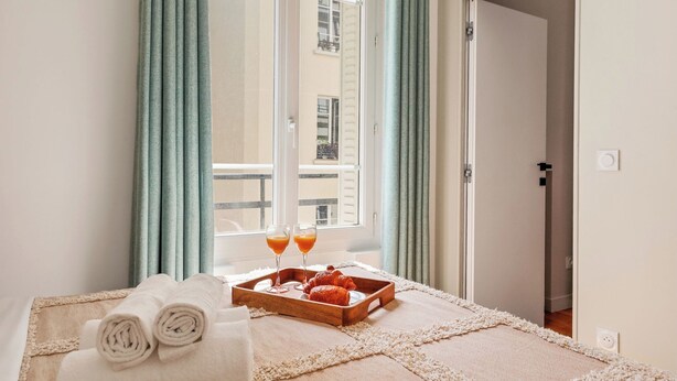 A hotel room with a bed, a tray with breakfast items, and a window with curtains. - Chic Flat near Opéra & Marais (Paris)