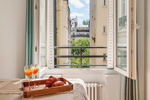 A window with a view of buildings, a radiator, and a tray with croissants and glasses of orange juice. - Chic Flat near Opéra & Marais (Paris)