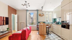 A modern apartment with a red sofa, a kitchen with a dining area, and a view of the city through an open door. - Chic Flat near Opéra & Marais (Paris)