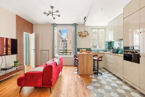 A modern apartment with a red sofa, a kitchen with a dining area, and a view of the city through an open door. - Chic Flat near Opéra & Marais (Paris)