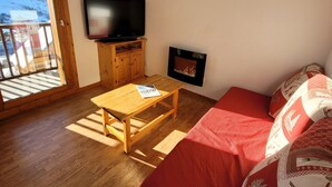 Ein Zimmer mit Holzboden, einem Sofa mit roten Kissen, einem an der Wand montierten Fernseher und einem Kamin.