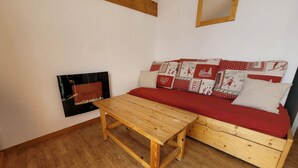 Ein gemütliches Zimmer mit einem Holztisch, einer Couch mit gemusterten Kissen und einem an der Wand befestigten Fernseher.