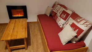 Ein gemütliches Zimmer mit einem Holztisch, einem roten Sofa mit gemusterten Kissen und einem Kamin.