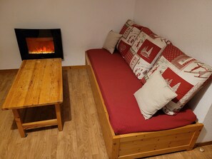 Ein gemütliches Zimmer mit einem Holztisch, einem roten Sofa mit gemusterten Kissen und einem Kamin.