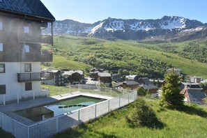 Ein Hotel mit Schwimmbad, umgeben von einem weißen Zaun, vor einer Bergkulisse und einem grünen Tal.