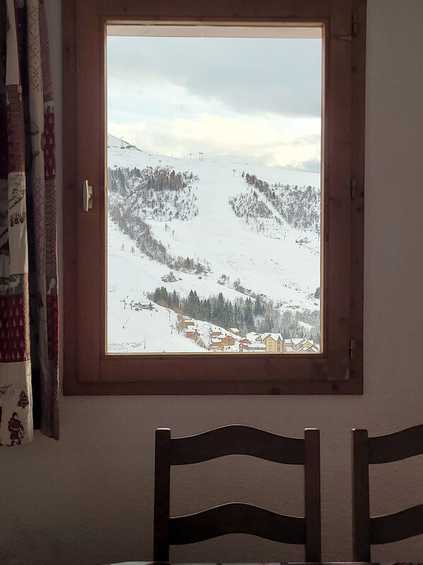 Ein Fenster mit Blick auf eine verschneite Landschaft, ein Holzsessel und ein Vorhang.