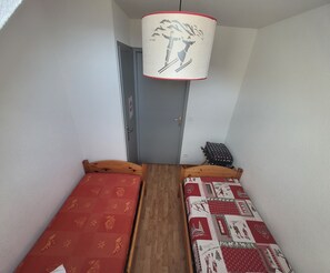Et lille rum med to senge i træ, en dør og en hængende lampe.