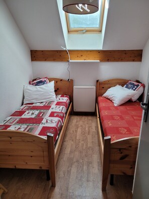 Ein kleiner, schmaler Raum mit zwei Holzbettgestellen, einer kleinen weißen Heizung und einem Oberlicht.