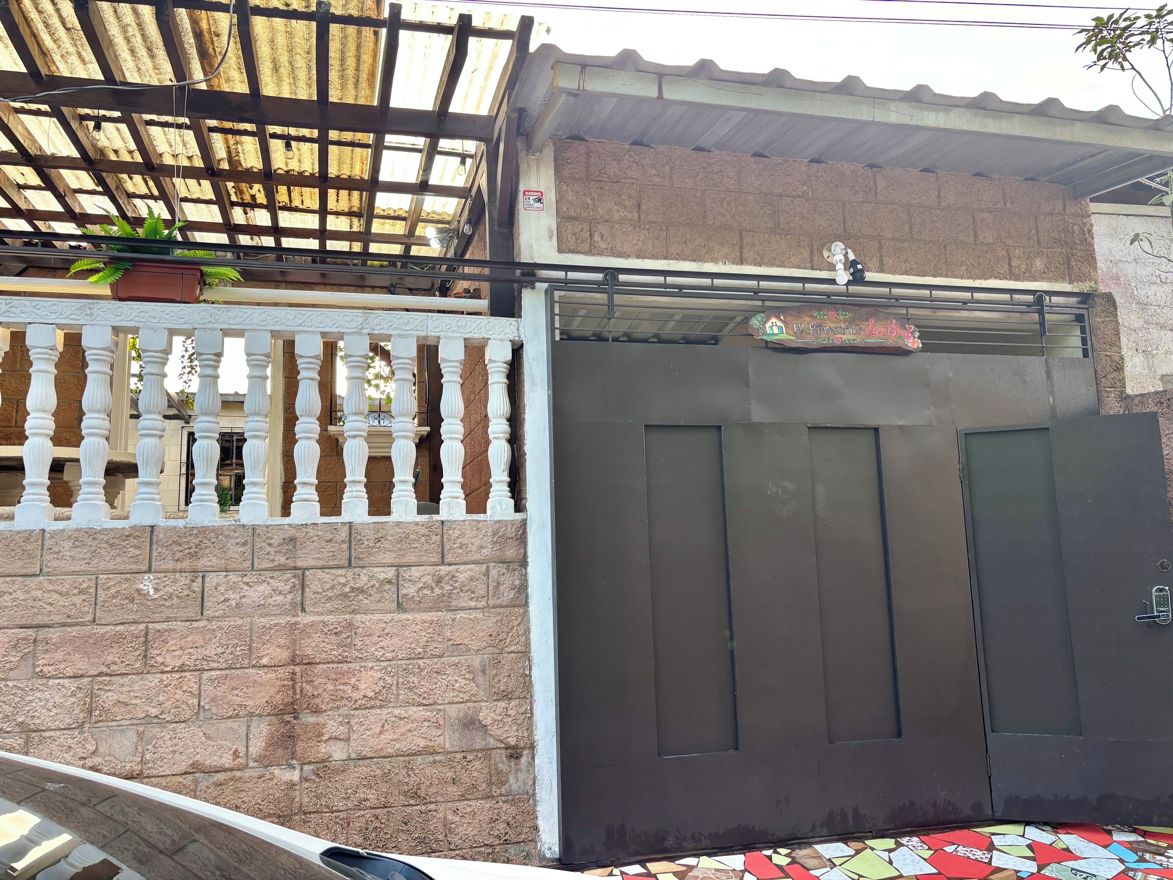 A gated entrance with a metal gate, a potted plant, and a sign above the gate.