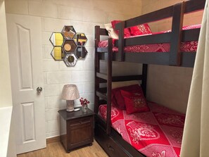 A bunk bed with red bedding, a nightstand with a lamp, and a wall-mounted hexagonal mirror. - Cozy 3-bedroom,1 car garage house in Apaneca perfect for a getaway (Apaneca)