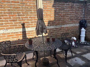Eine Terrasse mit einem runden Tisch, vier Stühlen, einem beigen Sonnenschirm und Topfpflanzen.