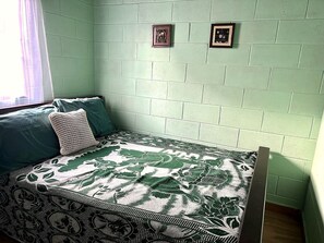 Ein Zimmer mit einem Bett, einem fenster mit Vorhängen und zwei gerahmten Bildern an der Wand.
