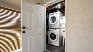 A laundry room with two stacked washing machines, a white door, and a wooden blind. - Rent The Crafty Mermaid, 2-bedroom house, yard, near Blue Heron dive area (West Palm Beach)