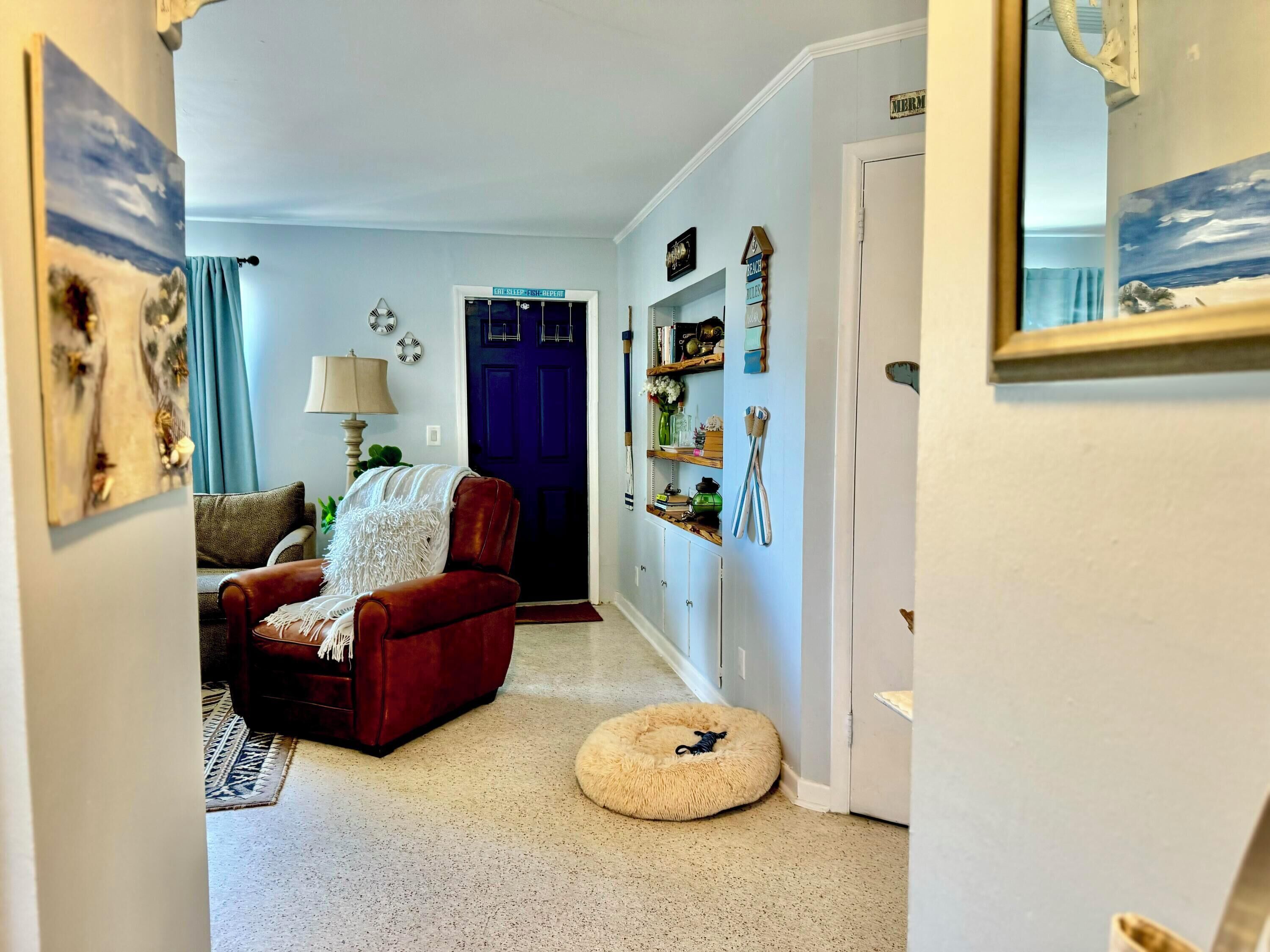 A living room with a red sofa, a white fluffy rug, a blue door, and a white wall with a clock and a mirror.