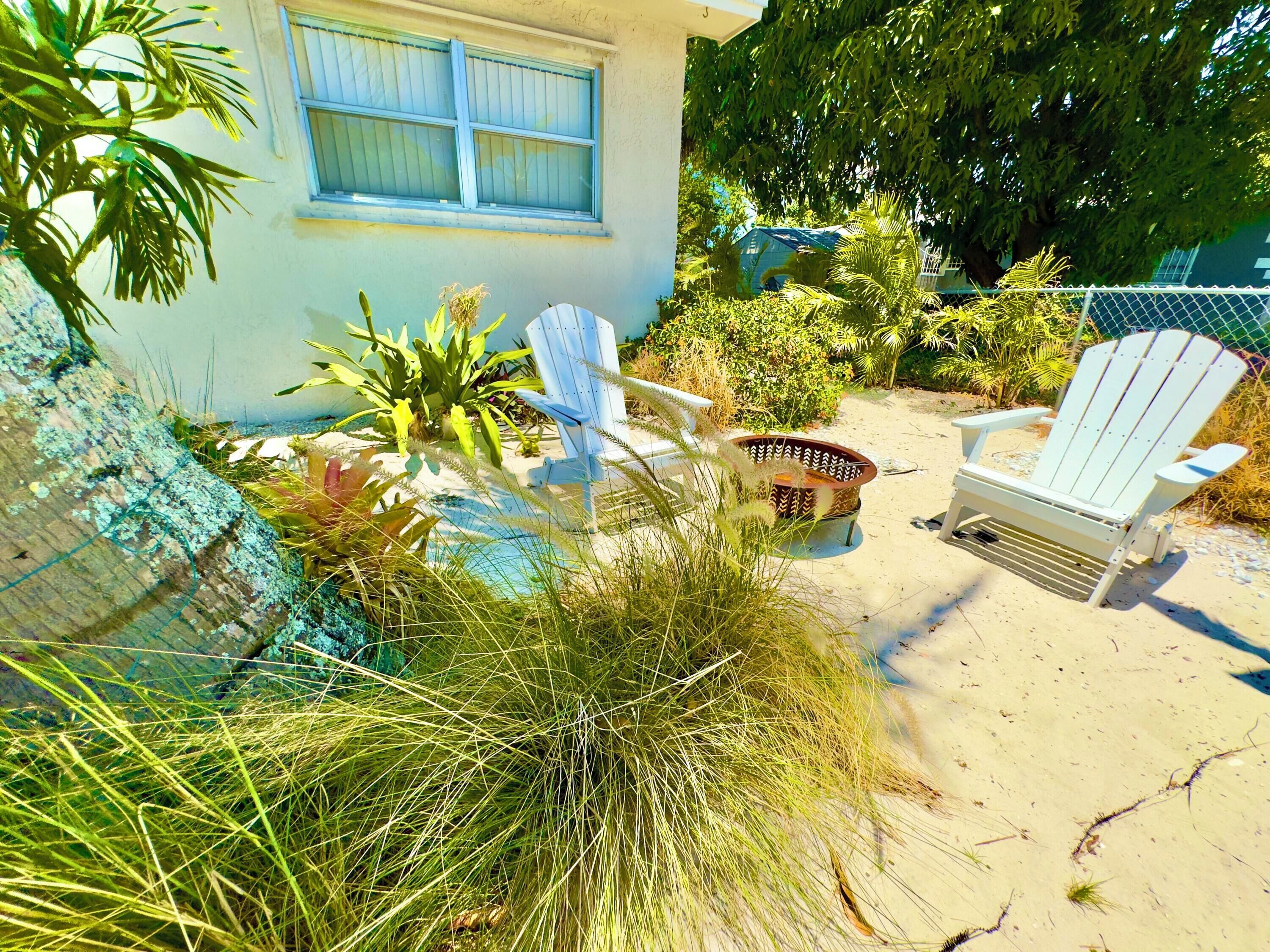 A beachside patio with two Adirondack chairs, a small table, and various plants.