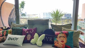 Un balcon offrant une vue sur le paysage urbain, agrémenté de différents coussins et d’un fauteuil suspendu.