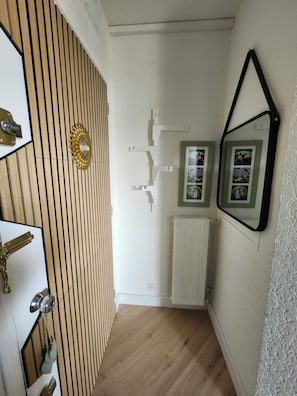 A hallway with wooden paneling, a radiator, and framed pictures on the wall. - A cozy little nest (Dax)
