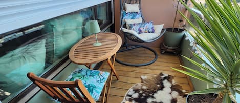 Uma varanda com mesa de madeira, cadeira suspensa, planta em vaso e tapete de pele.