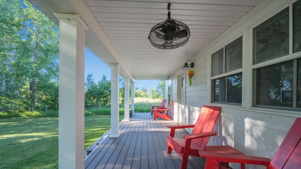 Un portico riparato con pavimento in legno, poltrone Adirondack rosse e una ventola a soffitto.