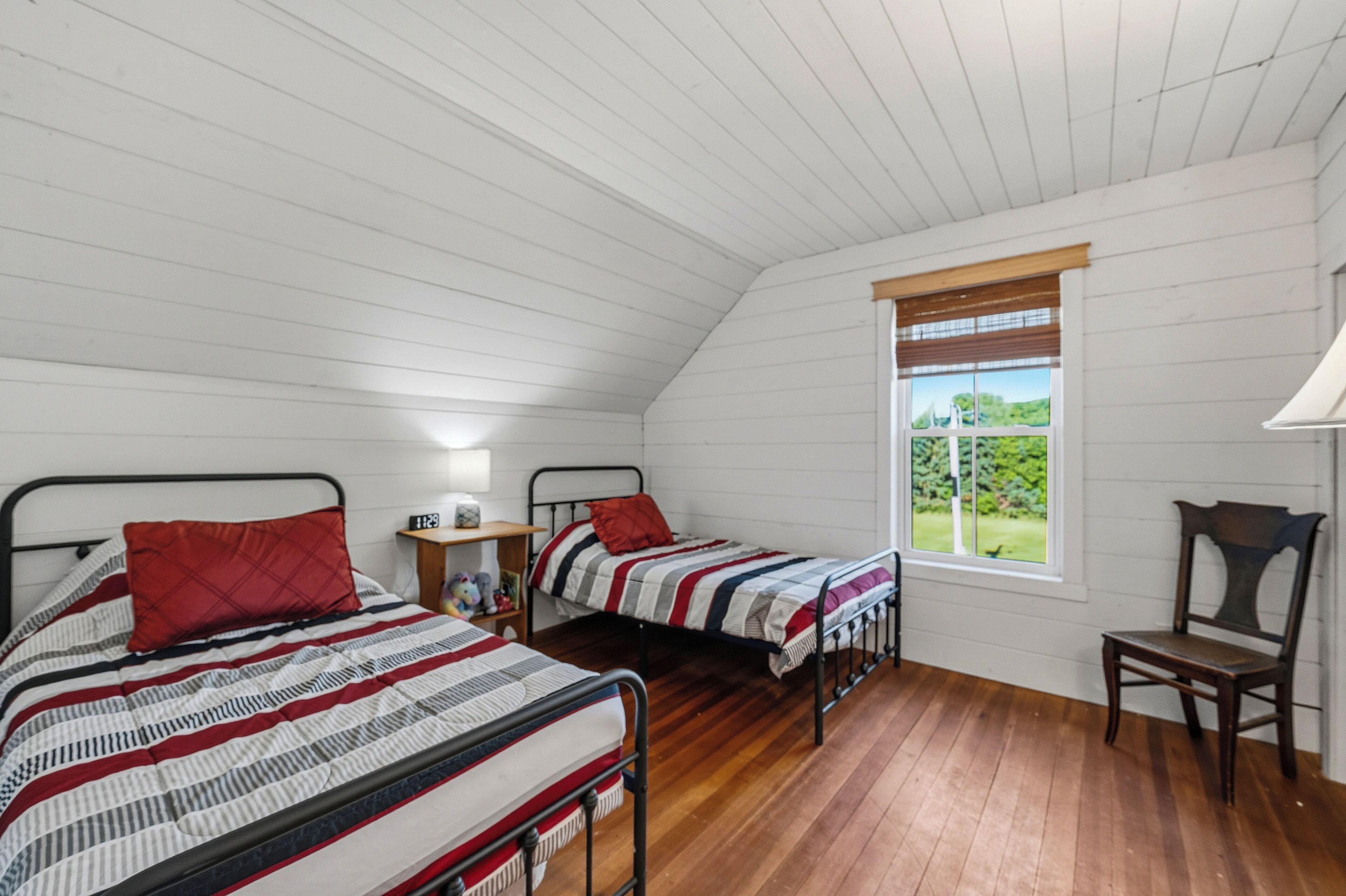 Una camera da letto con due letti, pavimento in legno, una finestra con vista e un comodino con una lampada.