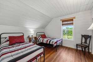 Quarto com duas camas, piso de madeira, janela com vista e mesa de cabeceira com abajur.