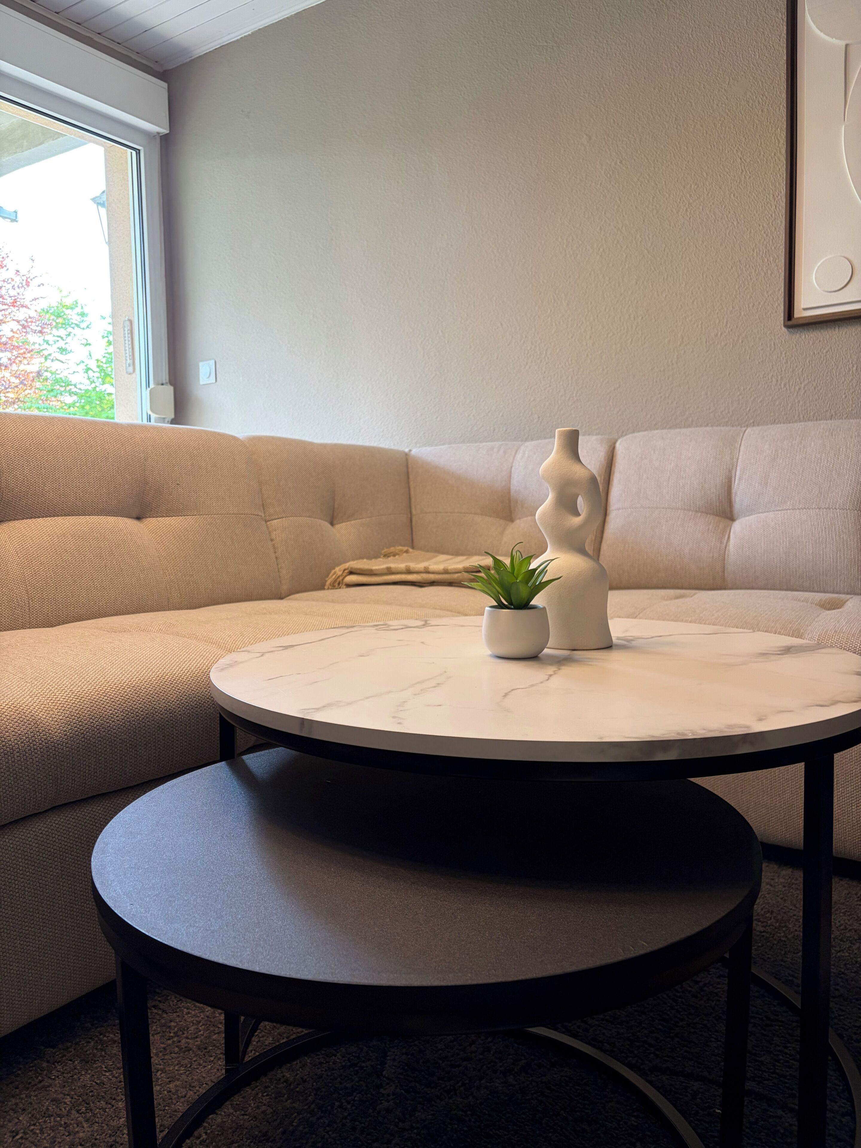 A modern living room with a beige sofa, a round marble table, and a potted plant.