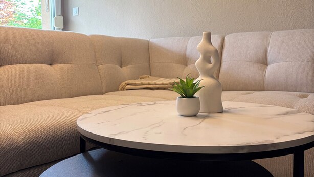Un salon moderne avec un canapé beige, une table ronde en marbre et une plante en pot.