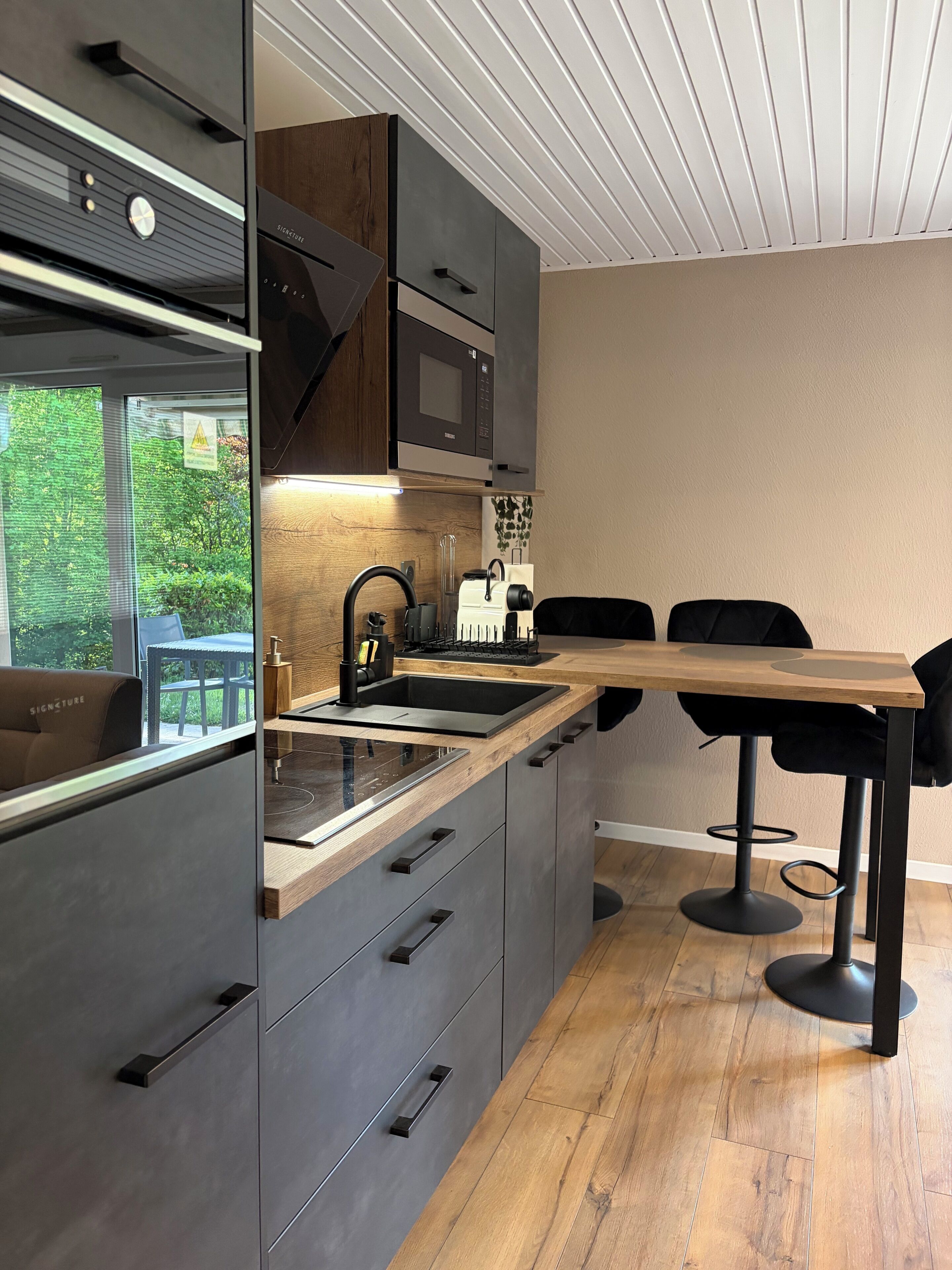 A modern kitchen with built-in appliances, a wooden countertop, and a dining area with black chairs.