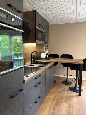A modern kitchen with built-in appliances, a wooden countertop, and a dining area with black chairs. - Le Cosy - Apartment with swimming pool near Lake Gerardmer (Gérardmer)