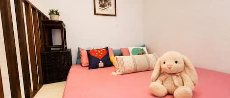 A bedroom with a pink bedspread, a plush toy, and a framed picture on the wall.