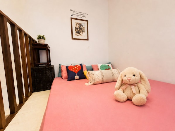 A bedroom with a pink bedspread, a plush toy, and a framed picture on the wall.
