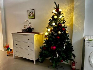 A Christmas tree with lights and ornaments, a white dresser, a small potted plant, and a toy horse.