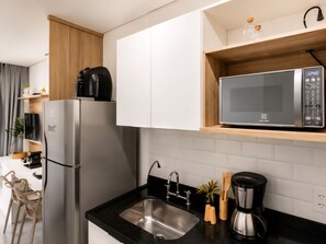 A modern kitchen with a stainless steel refrigerator, a microwave, a sink, and a coffee maker. - Studio Brooklin, EXPO (São Paulo)