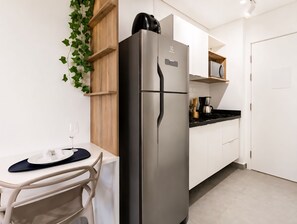A modern kitchen with a stainless steel refrigerator, a dining table with chairs, and a coffee maker on the counter. - Studio Brooklin, EXPO (São Paulo)